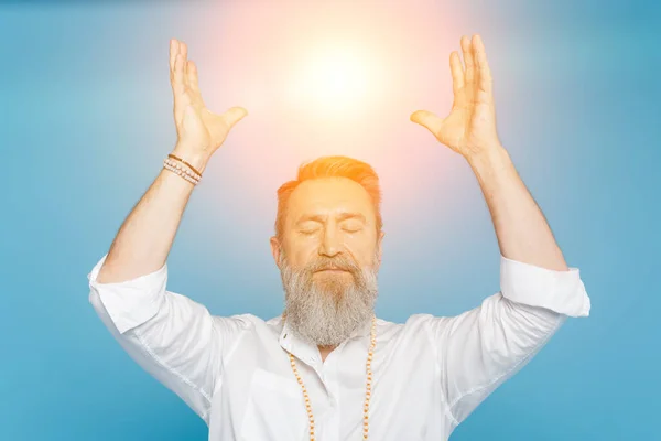 Master guru meditating with closed eyes and raised hands near shining aura isolated on blue — Stock Photo