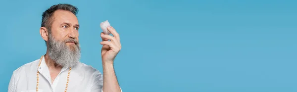 Senior spiritual guru meditating with selenite stone isolated on blue, banner — Stock Photo