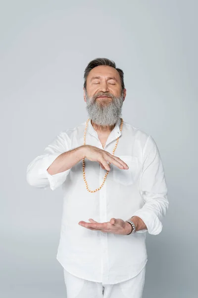 Gurú barbudo entrenador gesto mientras medita con los ojos cerrados aislados en gris - foto de stock