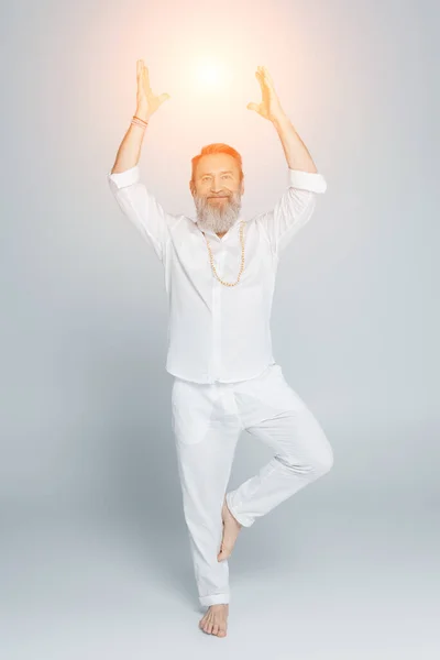 Full length of yoga guru meditating in tree pose near shining chakra on grey — Stock Photo