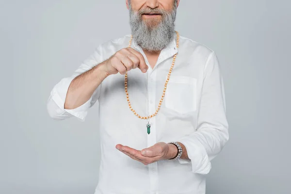 Partial view of bearded spiritual guru holding dowsing pendulum isolated on grey — Stock Photo