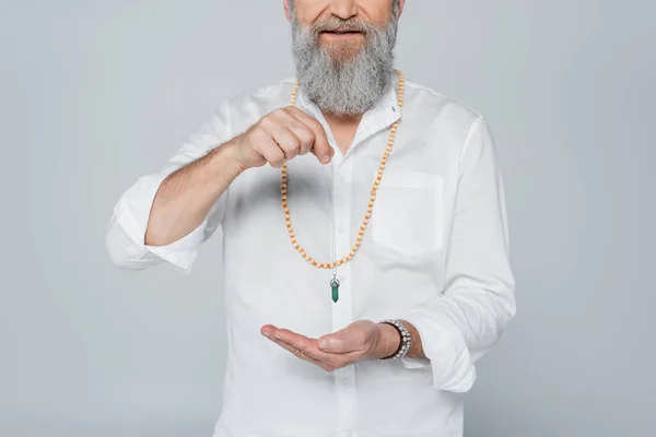 Visão parcial de guru espiritual barbudo segurando pêndulo dowsing isolado em cinza — Fotografia de Stock