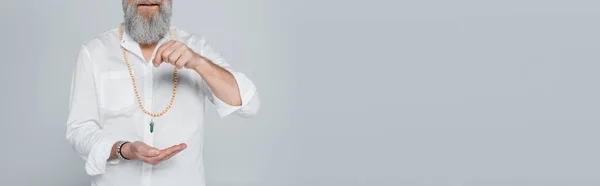 Vista recortada de gurú mentor en camisa blanca sosteniendo péndulo de radiestesia aislado en gris, bandera - foto de stock
