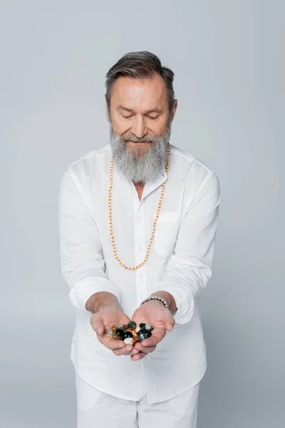 Senior guru master with handful of meditation stones isolated on grey — Stock Photo