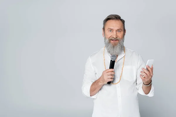 Motivational guru with mobile phone talking in microphone isolated on grey — Stock Photo