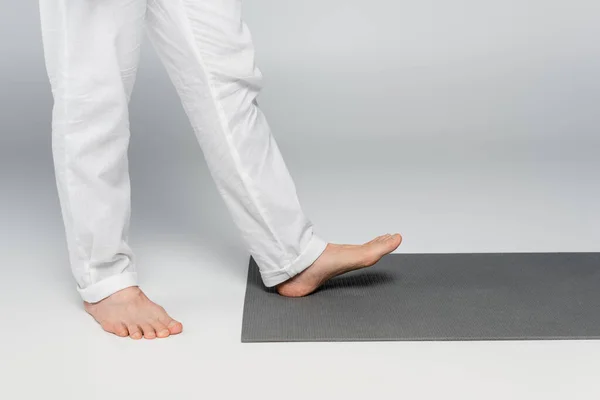 Cropped view of barefoot guru man stepping on yoga mat on grey — Stock Photo