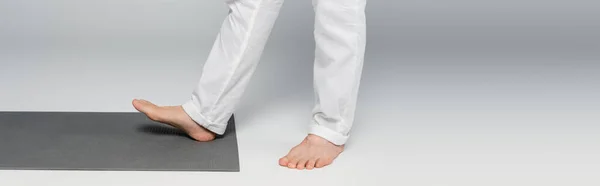 Visión parcial de gurú descalzo entrenador pisando alfombra de yoga en gris, bandera - foto de stock