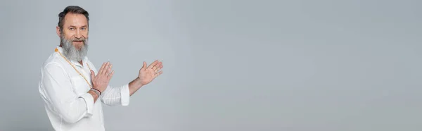 Bearded master guru in white shirt looking at camera and pointing with hands isolated on grey, banner — Stock Photo