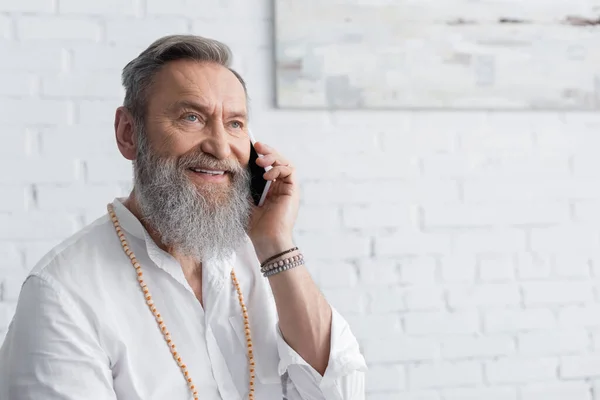 Glücklicher Meister-Guru in Perlen, der zu Hause auf dem Smartphone spricht — Stockfoto