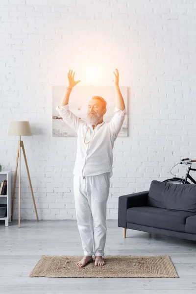 Full length of senior yoga master meditating in tree pose with raised hands near shining aura — Stock Photo