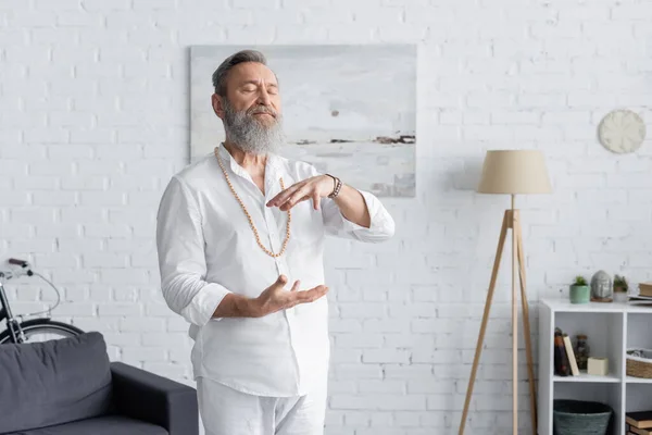 Entrenador espiritual en ropa blanca mostrando gesto de energía mientras medita con los ojos cerrados - foto de stock