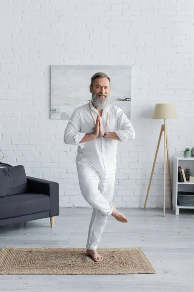 Comprimento total do homem guru descalço meditando com as mãos orando em pose de árvore em casa — Fotografia de Stock