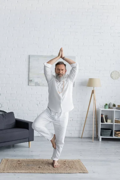 Älterer bärtiger Mann zeigt Anjani Mudra mit erhobenen Händen, während er in Baumpose meditiert — Stockfoto