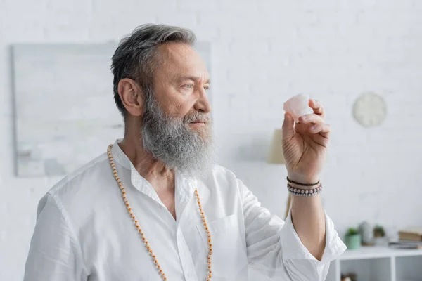 Maestro espiritual sénior en pulseras de cuentas meditando con piedra selenita - foto de stock