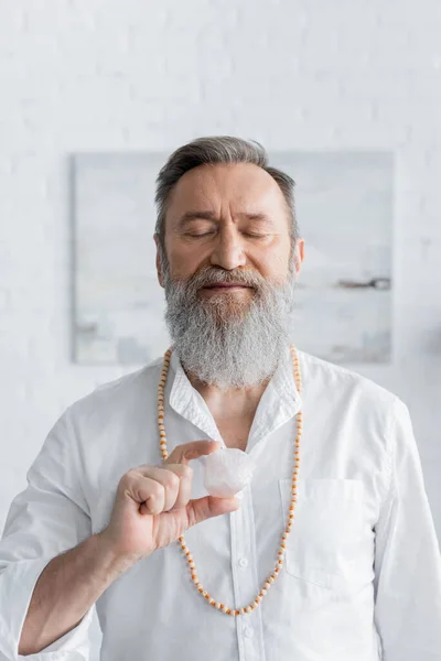 Bearded guru man meditating with closed eyes and selenite stone at home — Stock Photo