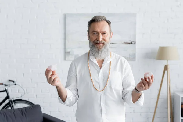 Guru mentor in beads holding selenite crystals and looking at camera — Stock Photo