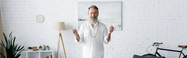 Bearded master guru holding selenite crystals and looking at camera in living room, banner — Stock Photo