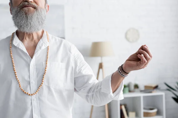 Cropped view of guru man in beads showing chin mudra while meditating at home — Stock Photo