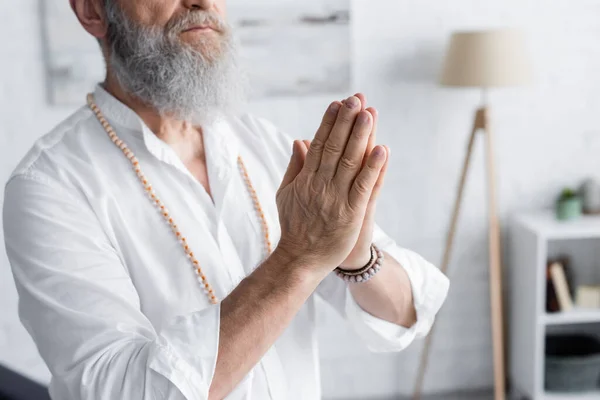 Partial view of senior man showing anjali mudra while meditating at home — Stock Photo