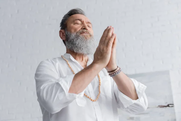 Low angle view of bearded guru man meditating with closed eyes and praying hands — Stock Photo