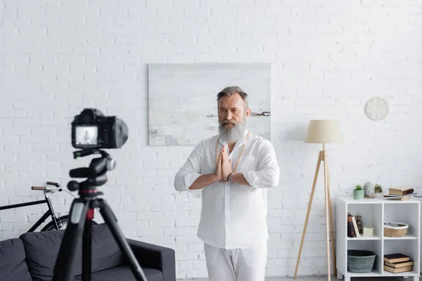 Guru mestre barbudo meditando com as mãos de oração na frente da câmera digital em casa — Fotografia de Stock