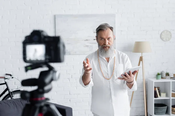 Master guru with digital tablet talking and pointing with hand near digital camera — Stock Photo