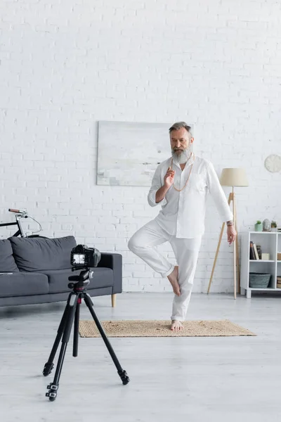 Senior yoga coach showing tree pose and prana mudra gesture in front of digital camera — Stock Photo