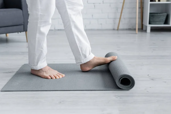 Vista parcial del hombre descalzo desenrollando la esterilla de yoga en casa - foto de stock
