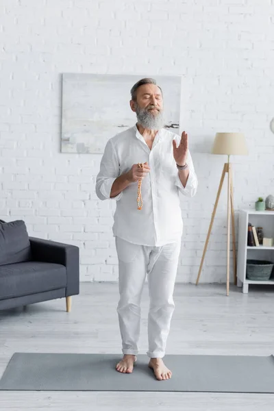 Comprimento total do tutor de ioga em roupas brancas meditando com contas mala em casa — Fotografia de Stock