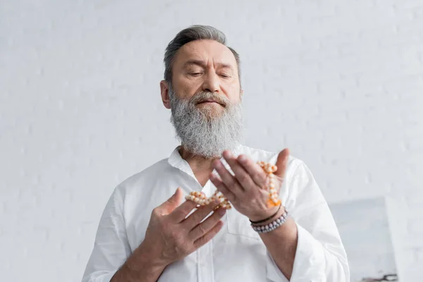 Low angle view of bearded guru man meditating with mala beads at home — Stock Photo