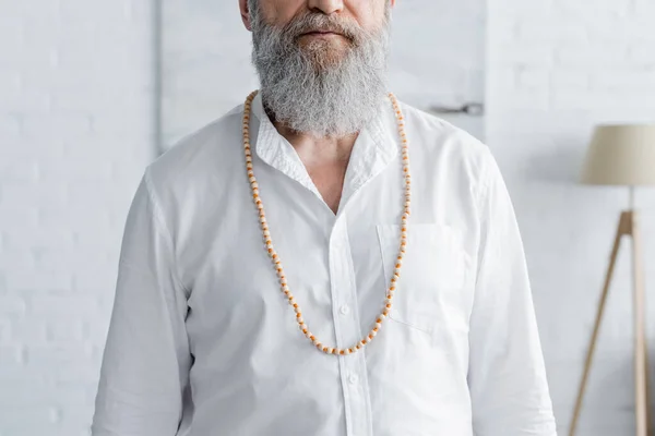 Vista cortada do homem guru barbudo em camisa branca e contas em casa — Fotografia de Stock