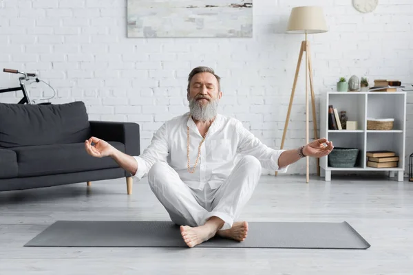 Bärtiger Guru-Trainer meditiert in lockerer Pose mit geschlossenen Augen im Wohnzimmer — Stockfoto