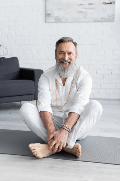 Entraîneur de yoga heureux dans des bracelets perlés assis dans la pose facile et regardant la caméra — Photo de stock