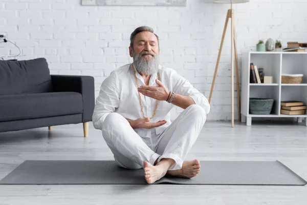 Senior master guru meditating in easy pose on yoga mat at home — Stock Photo