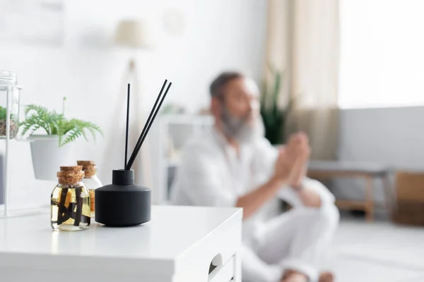 Selective focus of aroma sticks and essential oils near master guru meditating on blurred background — Stock Photo