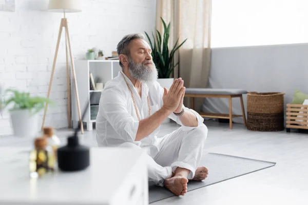 Maestro di yoga senior meditando in posa facile con le mani di preghiera su primo piano sfocato — Foto stock