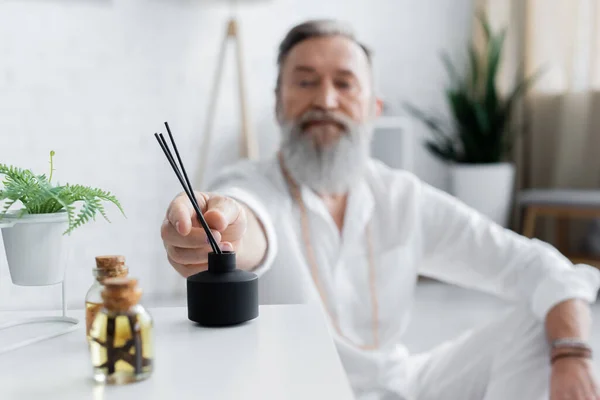 Selective focus of essential oils and diffuser with aroma sticks near blurred healing guru — Stock Photo