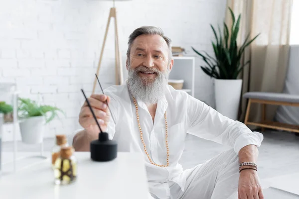 Feliz maestro de la curación sosteniendo palo de aroma cerca de aceites perfumados en primer plano borrosa - foto de stock