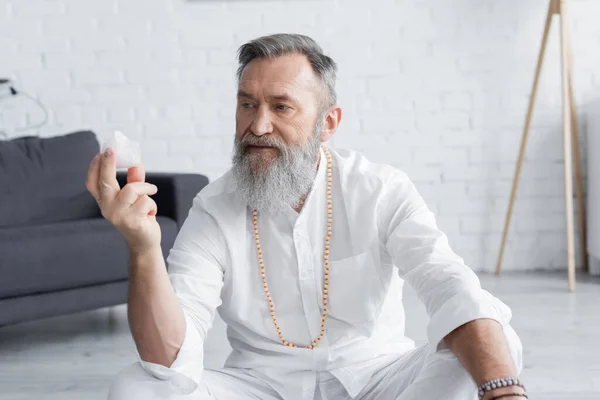 Guru espiritual sênior em contas meditando com cristal de selenita em casa — Fotografia de Stock