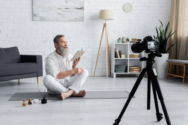 Yoga master reading manual while sitting in easy pose near essential oils and digital camera — Stock Photo