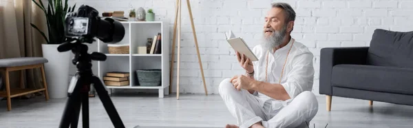 Bearded yoga coach reading manual in front of digital camera at home, banner — Stock Photo