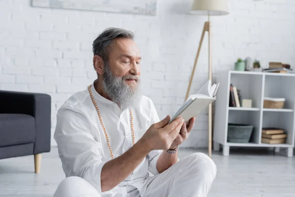 Meister-Guru in weißen Kleidern und Perlen liest Buch zu Hause — Stockfoto