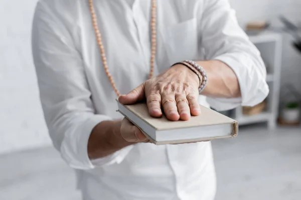 Partial view of spiritual mentor meditating with book on blurred background — Stock Photo