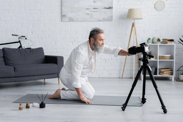 Yoga coach adjusting digital camera near aroma sticks and flavored oils at home — Stock Photo