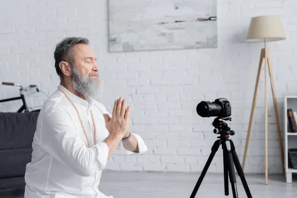 Mastermind guru meditating with closed eyes and praying hands near digital camera — Stock Photo