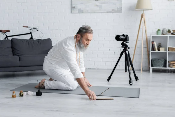 Yoga-Trainerin in weißer Kleidung hält Duftstäbchen neben Digitalkamera und aromatisierten Ölen — Stockfoto