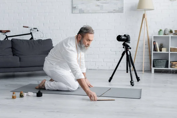 Yoga coach in vestiti bianchi che tengono bastoncini aroma vicino alla fotocamera digitale e oli aromatizzati — Foto stock