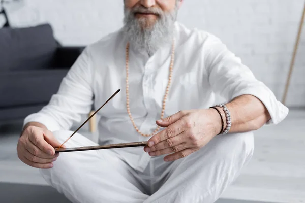 Partial view of guru man in white clothes and beaded bracelets holding aroma stick — Stock Photo