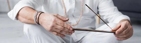 Vista recortada del hombre gurú en pulseras de cuentas que sostienen palo de aroma, bandera - foto de stock