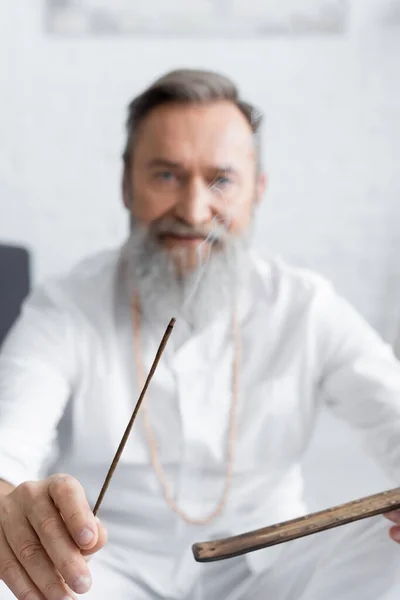 Guru ayurvédico desfocado segurando vara aroma ardente em casa — Fotografia de Stock